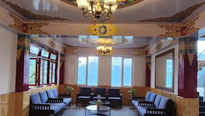 A room with a traditional design, featuring a central chandelier, wooden benches, and large windows. - Voyage Royal Retreat (Gangtok)