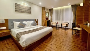A hotel room with a large bed, a desk with two chairs, a small table with a vase, and a wall-mounted shelf. - Voyage Royal Retreat (Gangtok)
