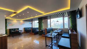 A modern dining area with booths and tables, large windows, and decorative wall art. - Voyage Royal Retreat (Gangtok)