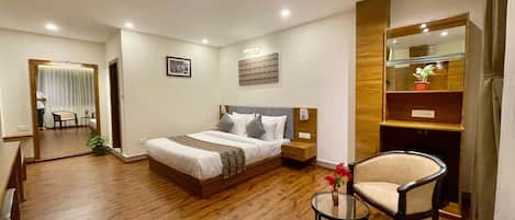 A hotel room with a bed, bedside table, chair, and a small table with a vase.