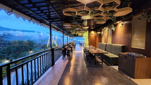 A restaurant with a long counter, wooden flooring, and a view of a mountainous landscape. - Voyage Royal Retreat (Gangtok)