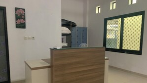Un mostrador de recepción con detalles de madera, un mueble azul con taquillas y una ventana con persiana estampada.