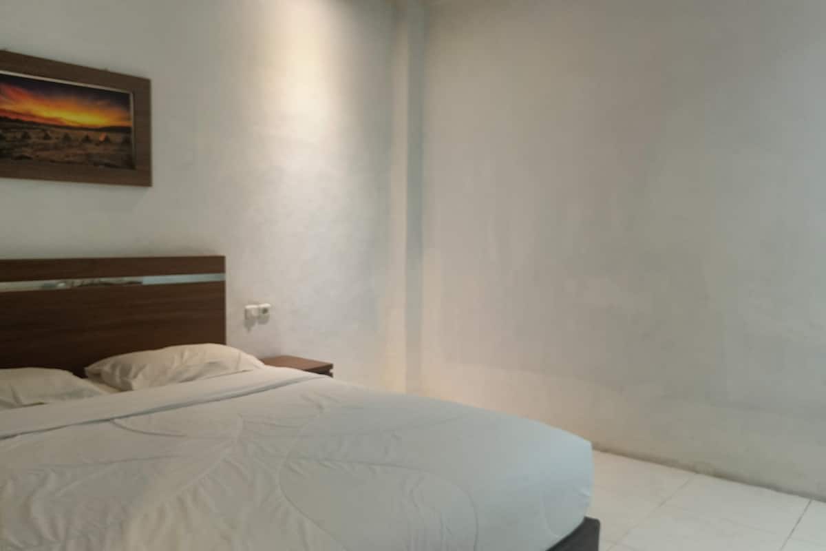 Ein Schlafzimmer mit einem Bett, einem Nachttisch, einem an der Wand hängenden Bild und einer schlichten Wand.