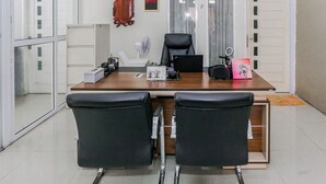A modern office with a wooden desk, two black leather chairs, a white fan, and a framed picture on the wall. - Hotel O Sman House (Bekasi)