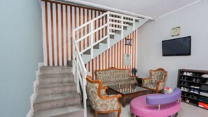 A staircase with a white railing leading to a landing. There are two patterned armchairs and a small round table with a purple cushion. A television is mounted on the wall above the armchairs. - Hotel O Sman House (Bekasi)