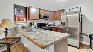 Cocina con encimeras de granito, electrodomésticos de acero inoxidable, gabinetes de madera y un cuadro en la pared.