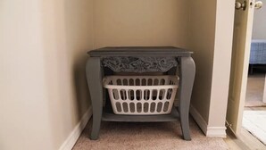 Una esquina con una mesa gris oscuro y una cesta blanca para ropa.