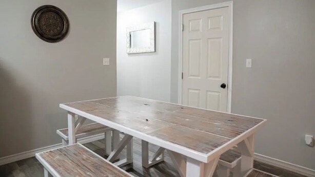 Una habitación con una puerta blanca, un reloj de pared y una mesa blanca con bancos.