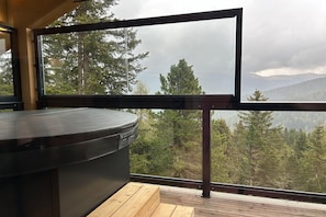 A modern room with a large window, a wooden deck, and a hot tub.