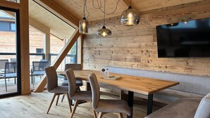 A modern interior with a wooden ceiling, a large flat-screen TV mounted on the wall, a wooden dining table with chairs, and a bench.
