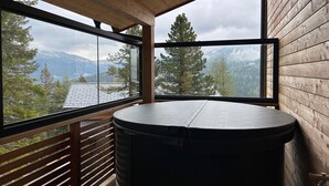 A room with a large window offering a mountain view, a round table, and wooden paneling.