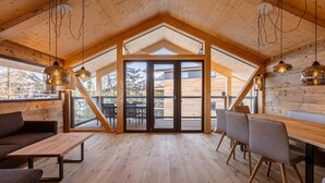 A spacious room with wooden floors, a large table, and chairs, and a view through glass doors to an outdoor deck.
