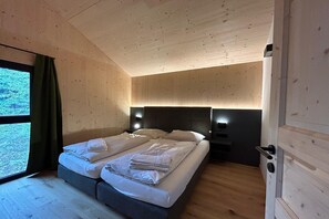 A bedroom with a bed, two bedside tables, a window with curtains, and wooden walls. - Nice chalet with sauna (Turrach)