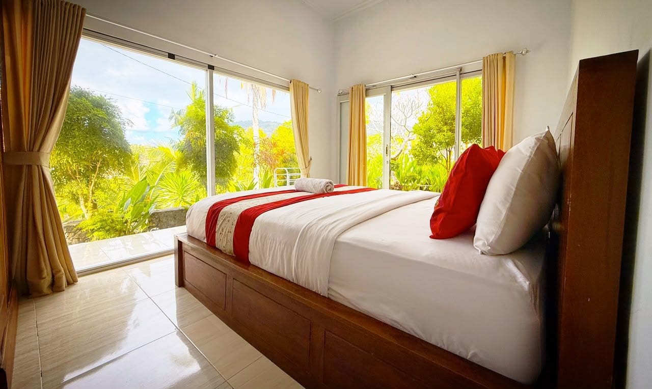 Ein Schlafzimmer mit einem großen Bett, einem Holzkopfende und Blick auf Grün durch die Fenster.