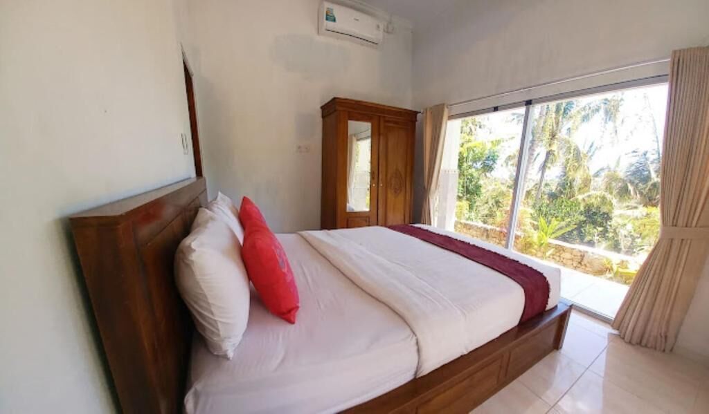 A bedroom with a bed, a wooden wardrobe, and a large window with a view of greenery.
