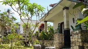 Un edificio tradicional con un acceso de pared de piedra, una estatua y abundante vegetación.