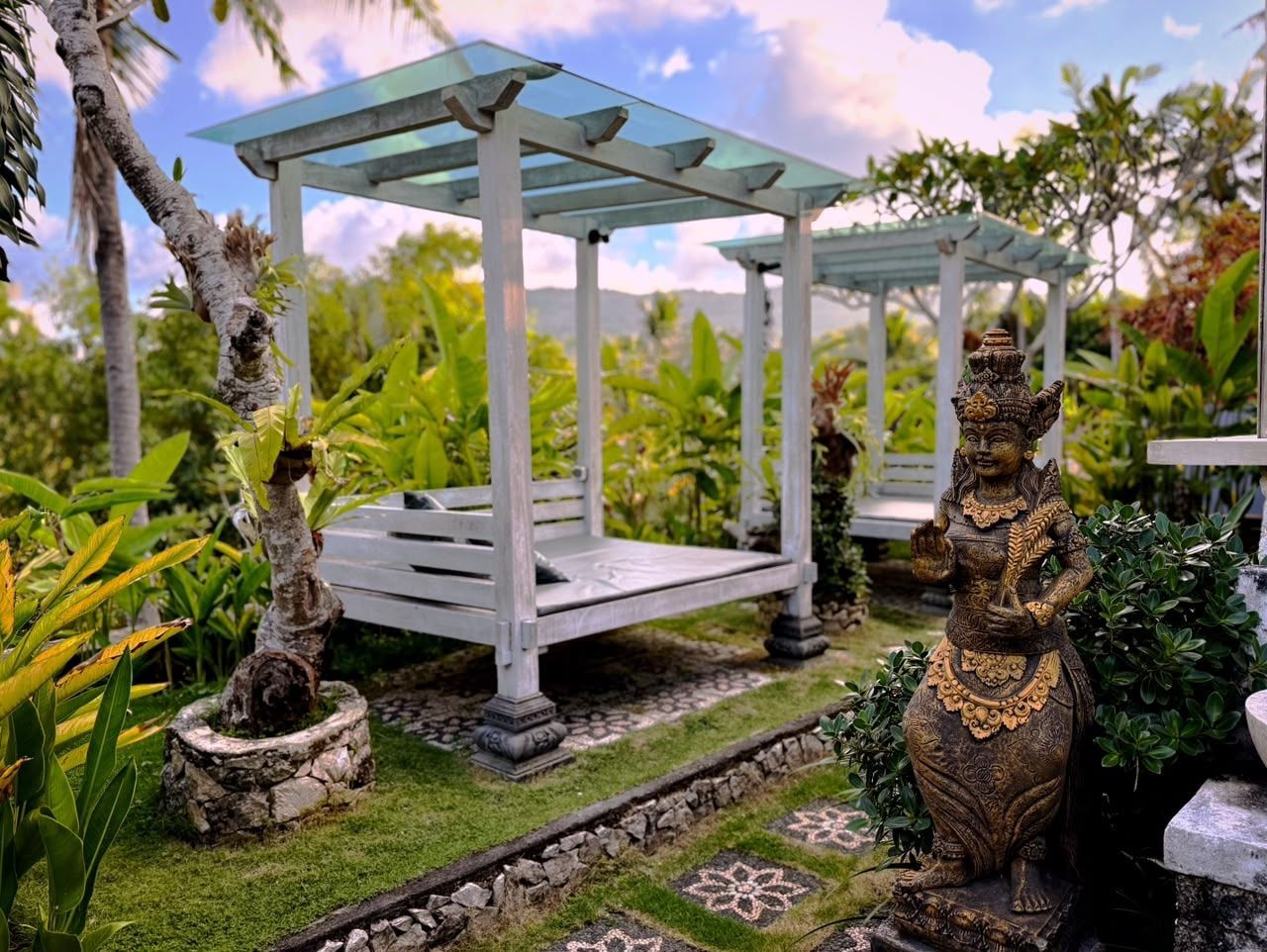 En pergola med glasloft, omgivet af eksotiske planter og en statue.