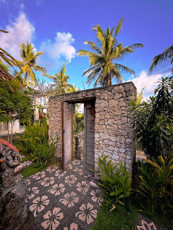 Un arc en pierre menant à un bâtiment, entouré de plantes tropicales et de palmiers.