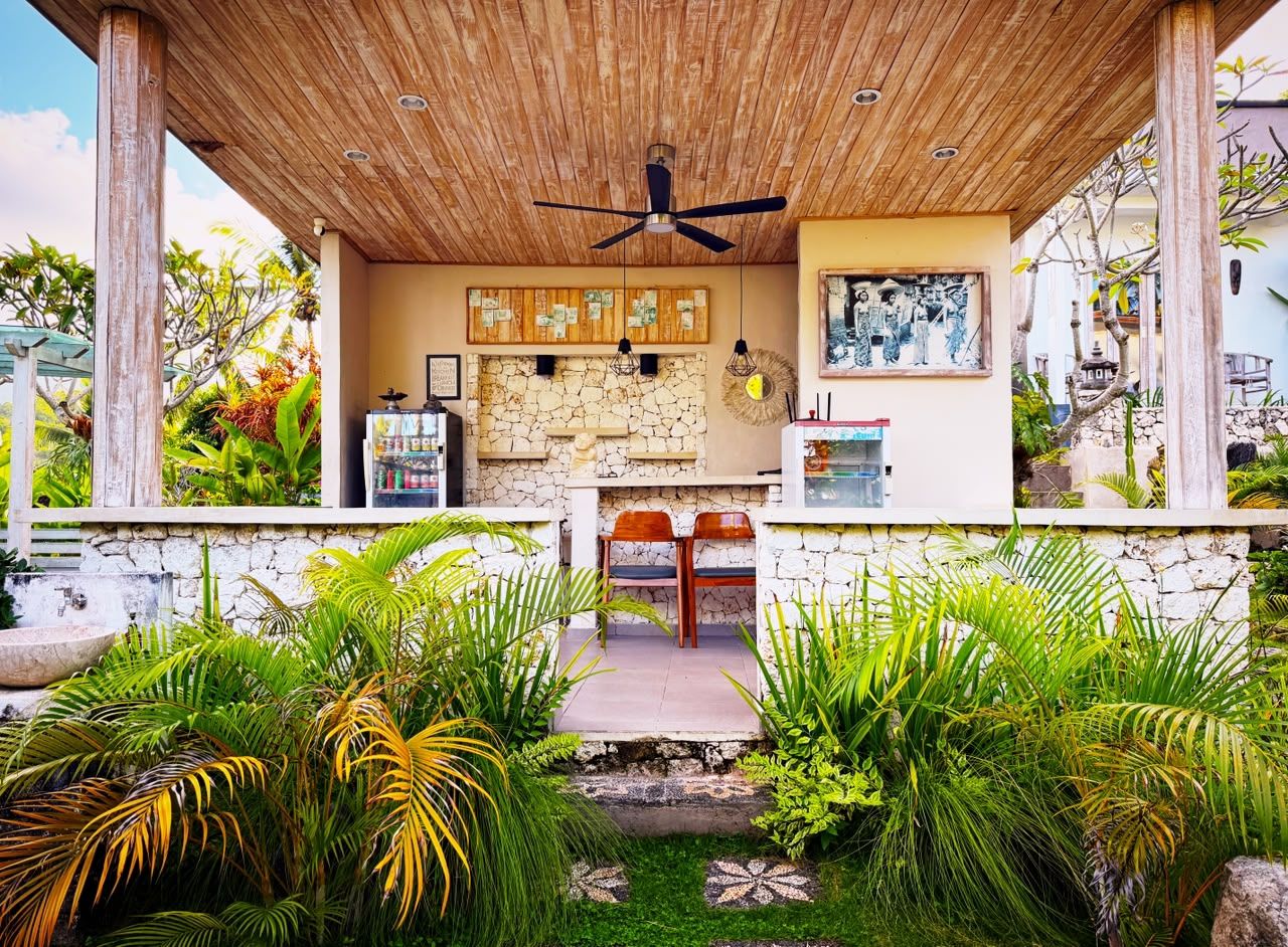 A covered outdoor seating area with a stone wall, wooden ceiling, and a ceiling fan.