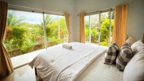 Un dormitorio con una cama grande, cortinas y vistas a un follaje exuberante.