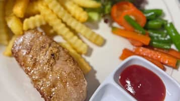 A plate with a piece of meat, French fries, mixed vegetables, and two dipping sauces.