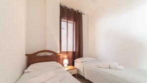 Una habitación con dos camas individuales, cabecero de madera, mesita de noche con lámpara y ventana con cortinas.