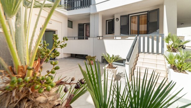 Un edificio residencial de varios niveles con balcones, plantas en macetas y una escalera.