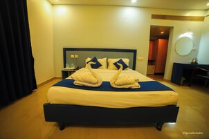 Habitación de hotel con cama, escritorio, silla, espejo y mesita de noche con una botella y teléfono.