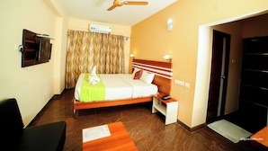 A hotel room with a bed, a desk, a chair, a ceiling fan, and a TV on the wall. - hotel bhaskara (Chittoor)