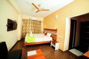 Habitación de hotel con una cama, un escritorio, una silla, un ventilador de techo y un televisor en la pared.