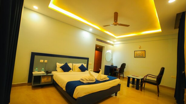 A hotel room with a bed, bedside table, chair, desk, and ceiling fan. - hotel bhaskara (Chittoor)