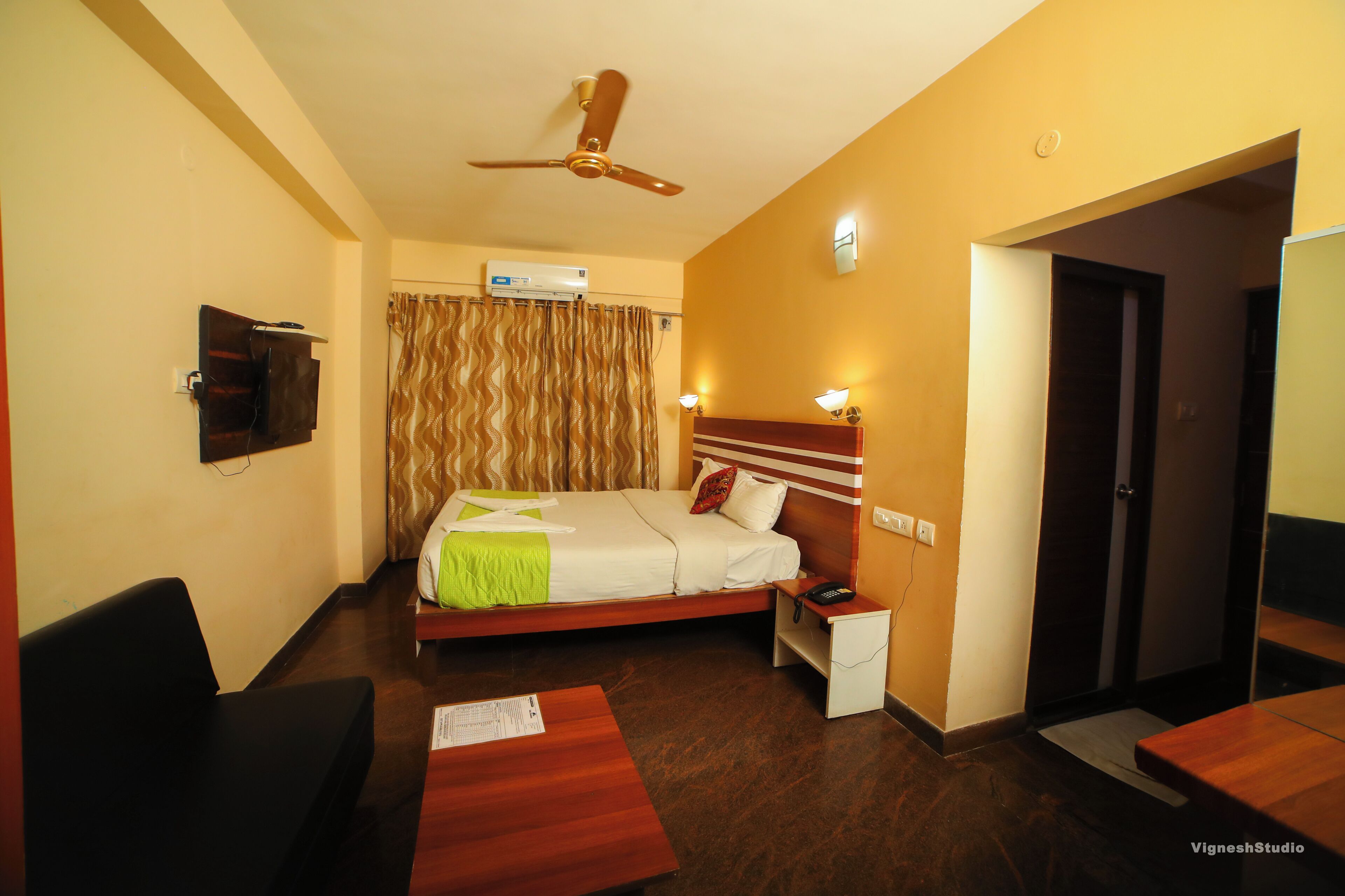 A hotel room with a bed, bedside table, nightstand, and a ceiling fan.