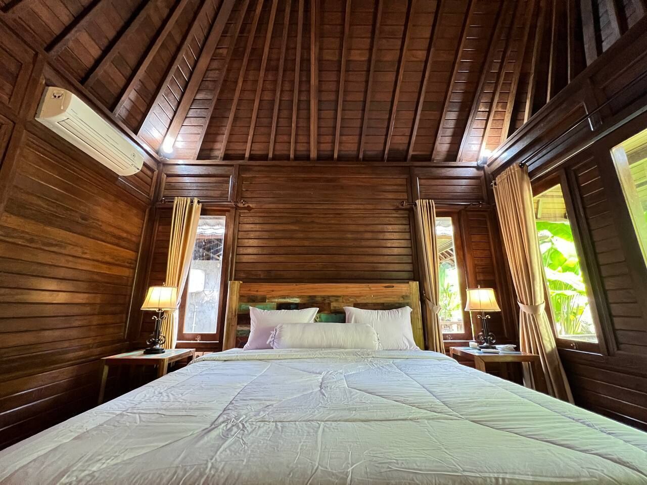 Una habitación con paneles de madera, una cama, dos lámparas de noche y ventanas con cortinas.