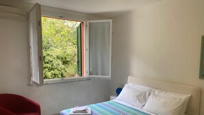 A bedroom with a bed, a red chair, and a window with curtains. - Green Oasis 1 (Lerici)