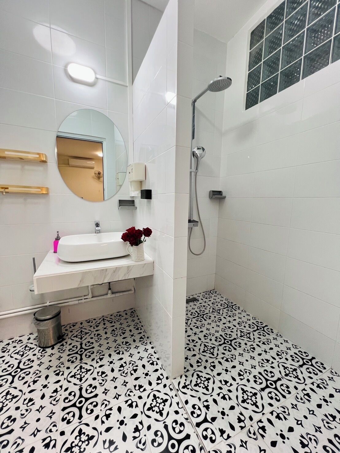 A modern bathroom with a white sink, mirror, and shower. The floor has a black and white patterned tile design.