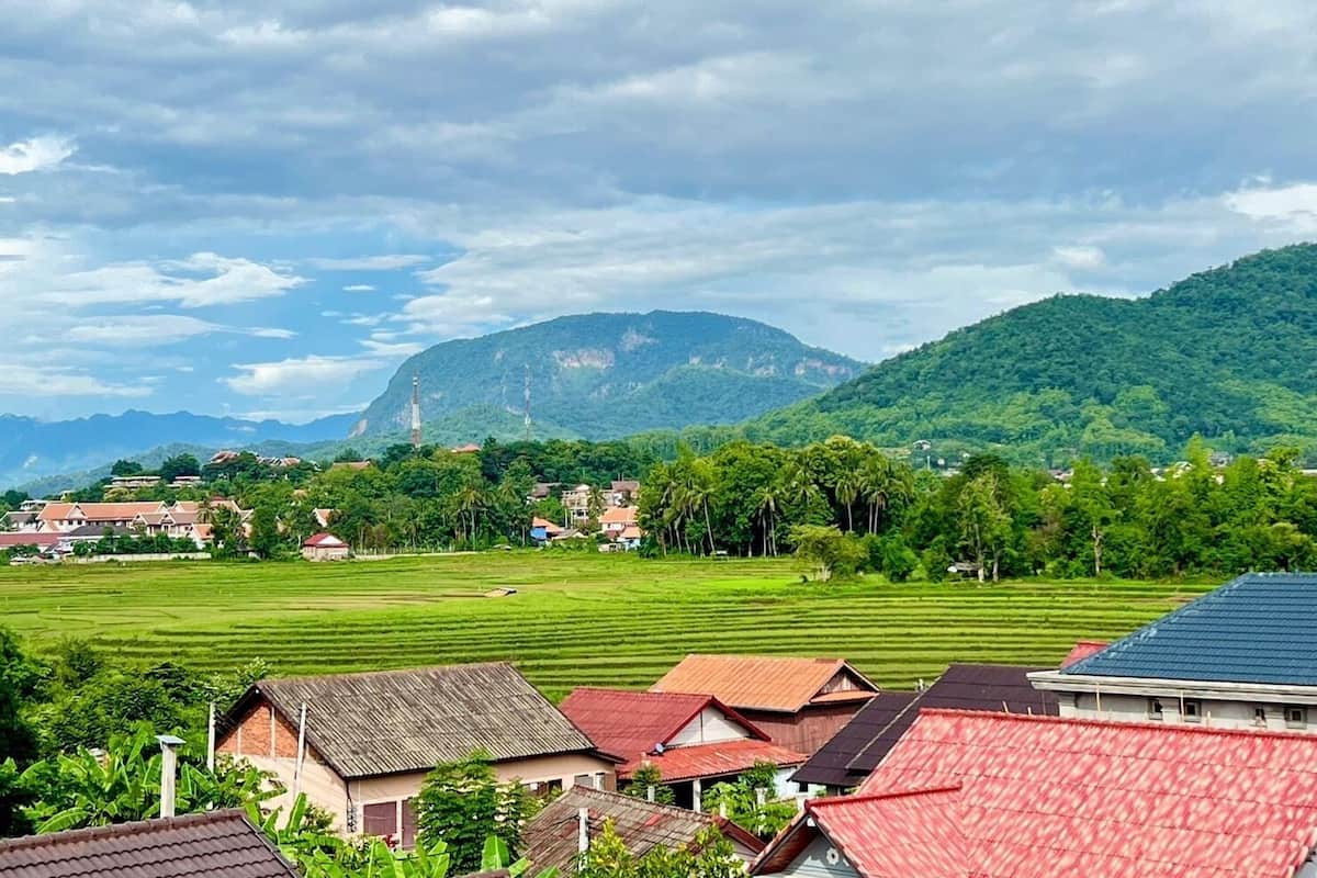 A rural landscape with houses, a large green field, and a mountain in the background.