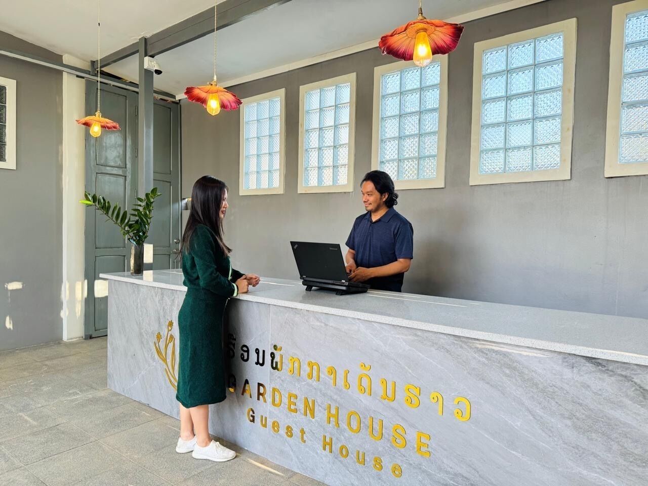 A reception desk with a marble top and a sign reading "Garden House Guest House".