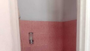 Une petite salle de bain avec des carreaux roses, des toilettes et un chauffe-eau.