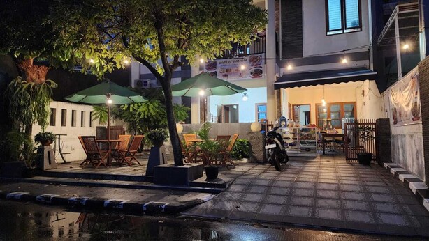 Un espace extérieur aménagé avec des tables et des chaises, une moto garée et l’entrée d’un bâtiment avec une enseigne.