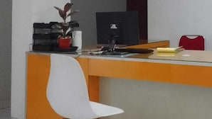 Un comptoir d’accueil avec une chaise blanche, un ordinateur et une plante.
