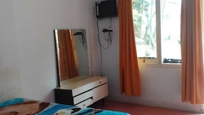 Une chambre à coucher avec un lit, un téléviseur fixé au mur et une fenêtre avec des rideaux.