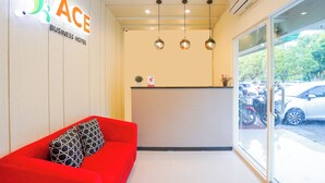 En hotellobby för affärsresenärer med en röd soffa, en receptionsdisk och utsikt över parkerade bilar genom stora fönster.