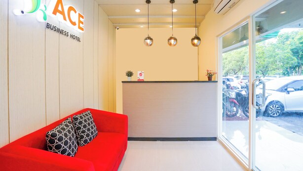A business hotel reception area with a red sofa, a reception desk, and a view of parked cars through large windows. - Hotel O Rungkut Near Its Surabaya Formerly Ace Business Hotel (Surabaya)