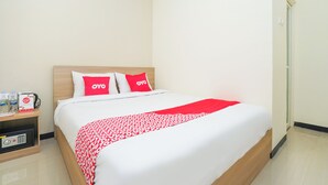 A hotel room with a bed, a bedside table with a kettle, and a red and white patterned blanket. - Hotel O Rungkut Near Its Surabaya Formerly Ace Business Hotel (Surabaya)