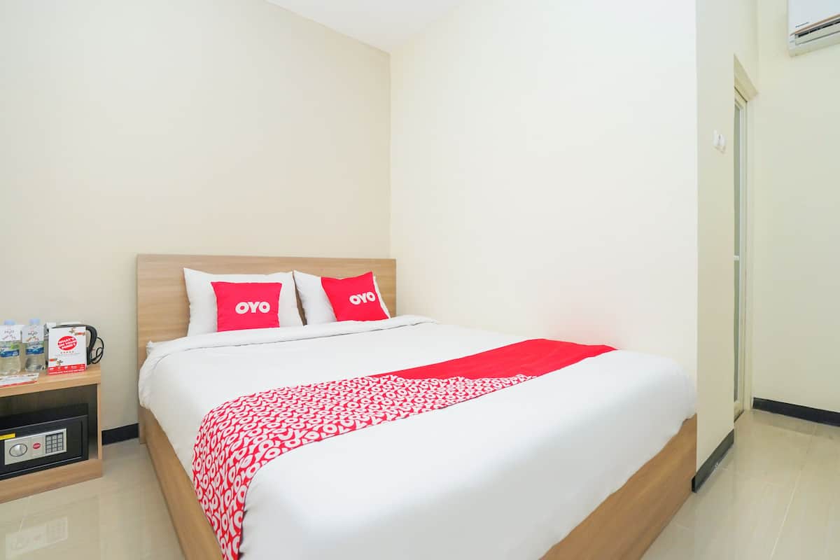 A hotel room with a bed, a bedside table with a kettle, and a red and white patterned blanket.