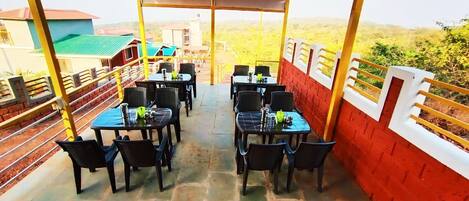 An outdoor dining area with tables and chairs, a red brick wall, and a view of the surrounding landscape.
