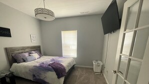 A bedroom with a bed, a nightstand, a window, a door, and a wall-mounted TV. - Charming 4-bedroom house with AC and WiFi in lovely Indianapolis (Indianapolis)