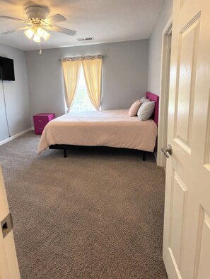Une chambre à coucher avec un lit, un ventilateur de plafond, une fenêtre avec des rideaux et une porte.