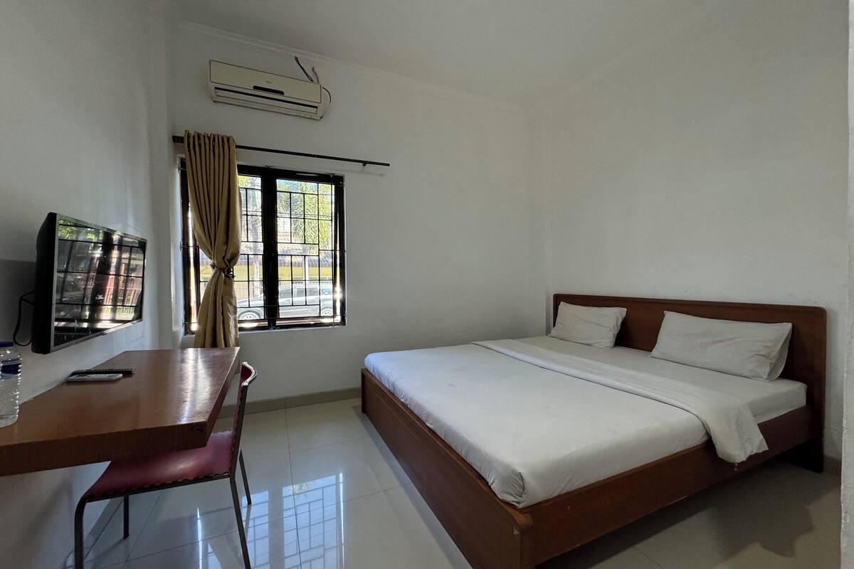 Habitación de hotel con cama, escritorio, silla, aire acondicionado y ventana con cortinas.