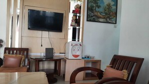 Ein Wohnzimmer mit an der Wand montiertem Fernseher, einer Mikrowelle, einem Laptop und einem Essbereich mit Stühlen und Tisch.